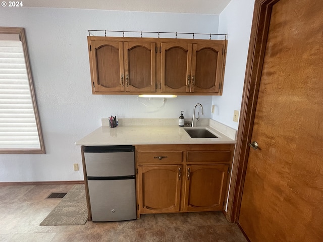 kitchen with visible vents, a sink, freestanding refrigerator, brown cabinetry, and light countertops