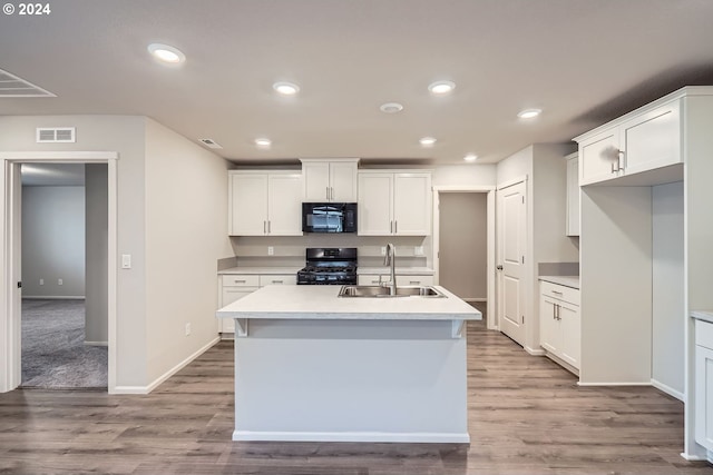 kitchen featuring sink, an island with sink, white cabinets, black appliances, and light wood-type flooring