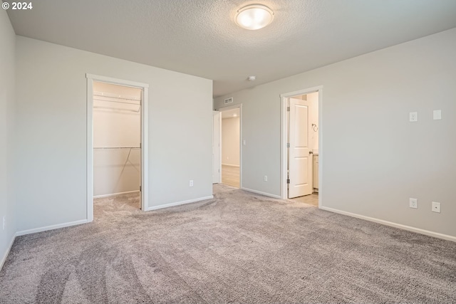 unfurnished bedroom featuring light carpet, a textured ceiling, a walk in closet, and a closet