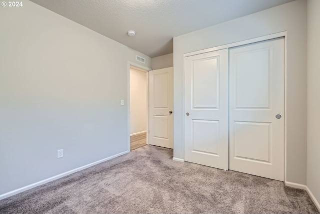 unfurnished bedroom with light colored carpet, a textured ceiling, and a closet