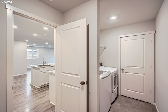 clothes washing area featuring light wood-type flooring, washer and clothes dryer, and sink