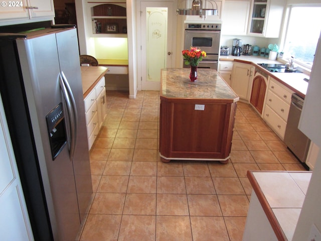 kitchen with sink, light tile patterned floors, a kitchen island, stainless steel appliances, and white cabinets