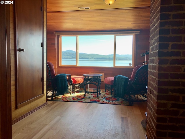 sitting room featuring wooden walls, a water and mountain view, and wood-type flooring