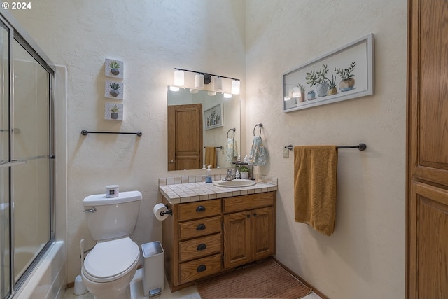 full bathroom featuring combined bath / shower with glass door, a textured wall, vanity, and toilet