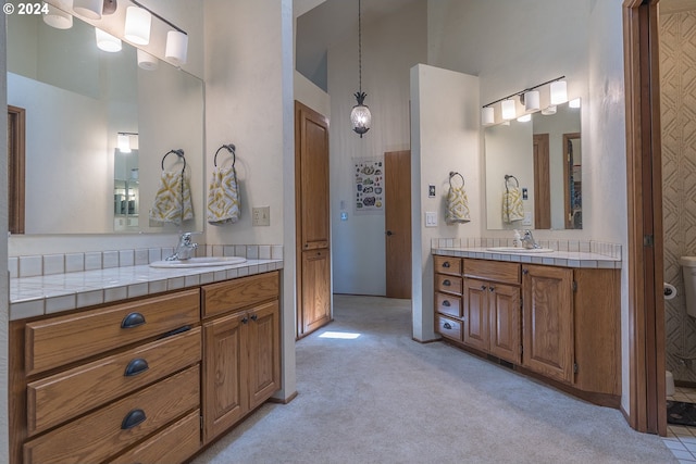 full bath with toilet, a high ceiling, two vanities, and a sink