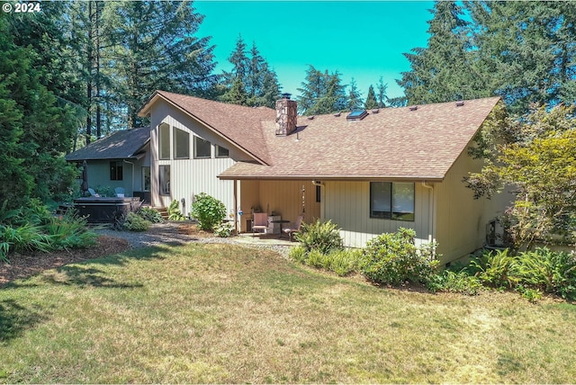 rear view of house featuring a shingled roof, a lawn, a chimney, and a patio