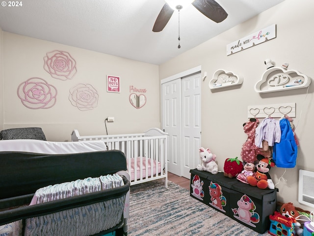 bedroom with a closet, ceiling fan, heating unit, hardwood / wood-style flooring, and a nursery area