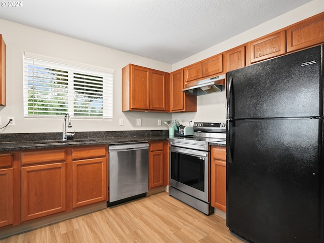 kitchen featuring sink, a textured ceiling, light hardwood / wood-style floors, stainless steel appliances, and dark stone countertops