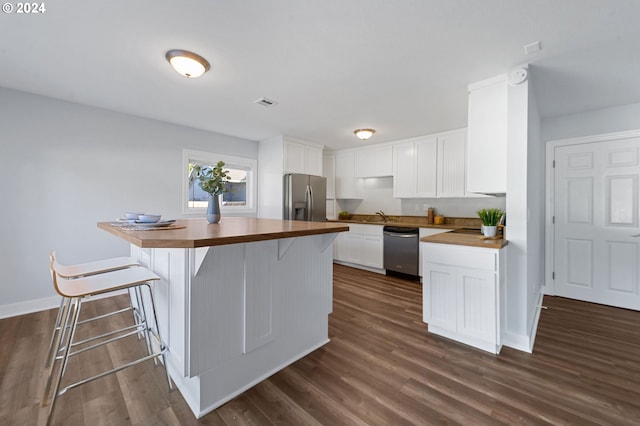 kitchen with appliances with stainless steel finishes, white cabinetry, a kitchen bar, dark hardwood / wood-style floors, and sink