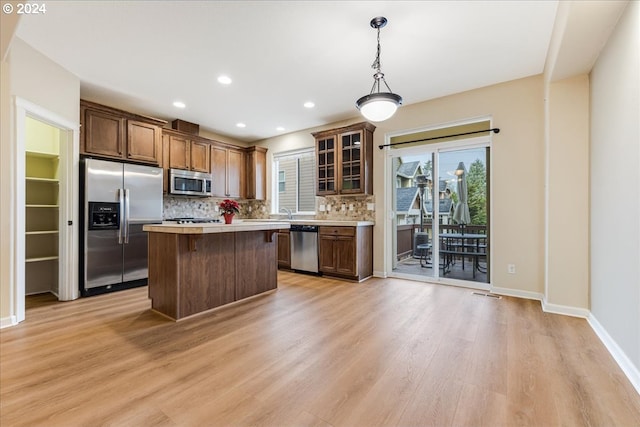 kitchen featuring light wood-type flooring, backsplash, stainless steel appliances, a center island, and hanging light fixtures