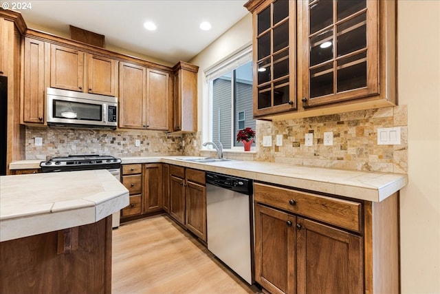 kitchen with appliances with stainless steel finishes, tasteful backsplash, sink, tile countertops, and light hardwood / wood-style floors