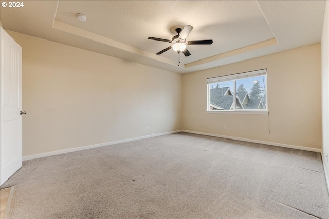 empty room with a raised ceiling, ceiling fan, and light colored carpet