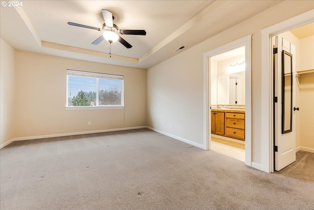 unfurnished bedroom featuring a raised ceiling, connected bathroom, a walk in closet, and light carpet