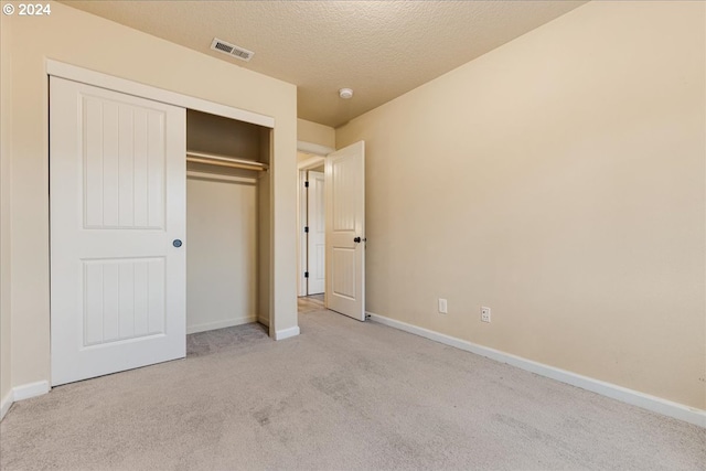 unfurnished bedroom with light colored carpet, a textured ceiling, and a closet