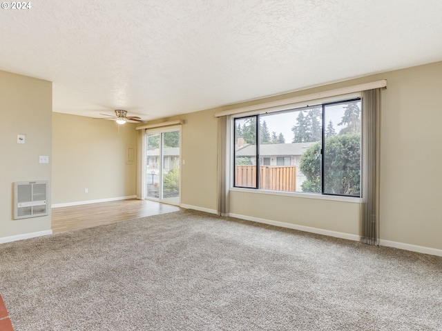 carpeted empty room with heating unit, ceiling fan, and a textured ceiling