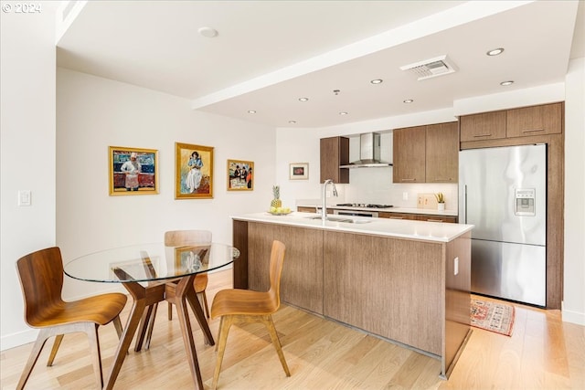 kitchen featuring sink, wall chimney exhaust hood, stainless steel appliances, light hardwood / wood-style flooring, and backsplash