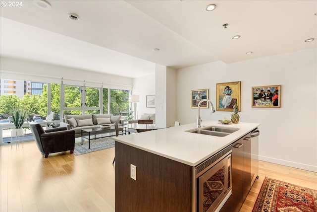 kitchen with dark brown cabinetry, light hardwood / wood-style flooring, a kitchen island with sink, and sink