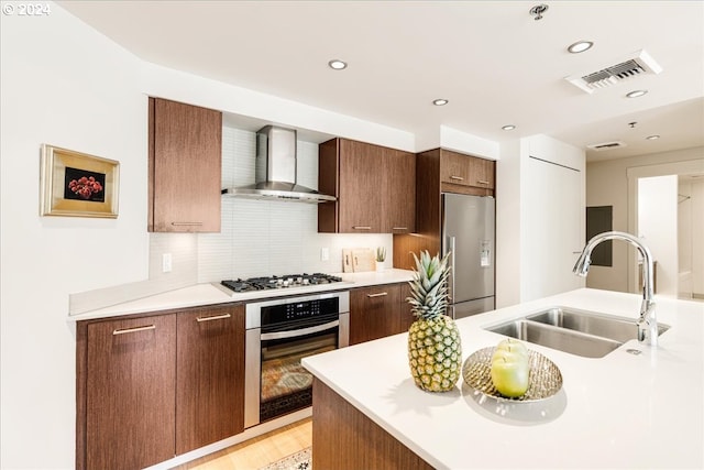 kitchen featuring appliances with stainless steel finishes, tasteful backsplash, sink, wall chimney range hood, and light hardwood / wood-style flooring