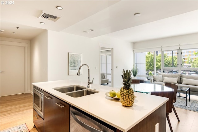 kitchen featuring a center island with sink, sink, light hardwood / wood-style flooring, dark brown cabinetry, and stainless steel appliances