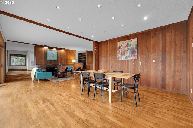 dining room featuring wooden walls, a brick fireplace, ornamental molding, and light wood-type flooring