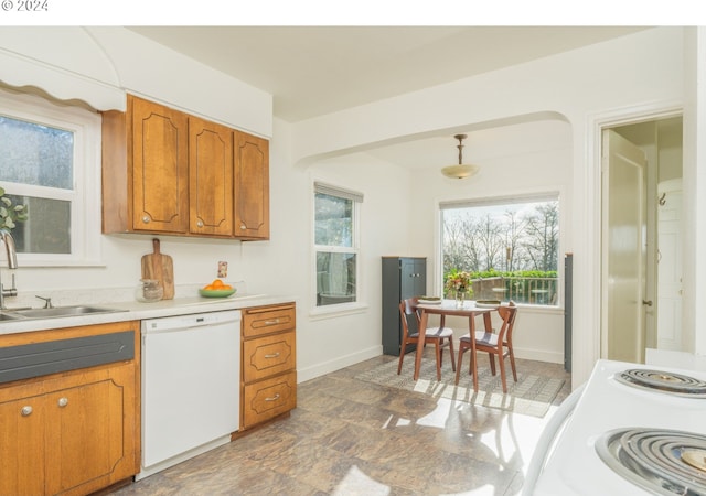 kitchen with white dishwasher, a sink, brown cabinetry, light countertops, and stone finish floor