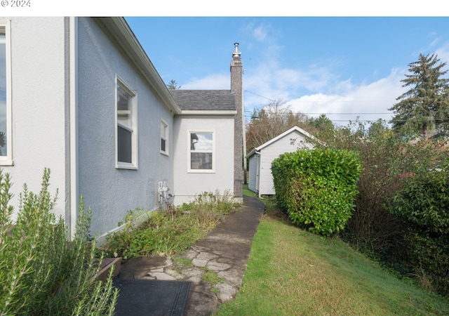 view of home's exterior with an outdoor structure, a shingled roof, a chimney, and stucco siding