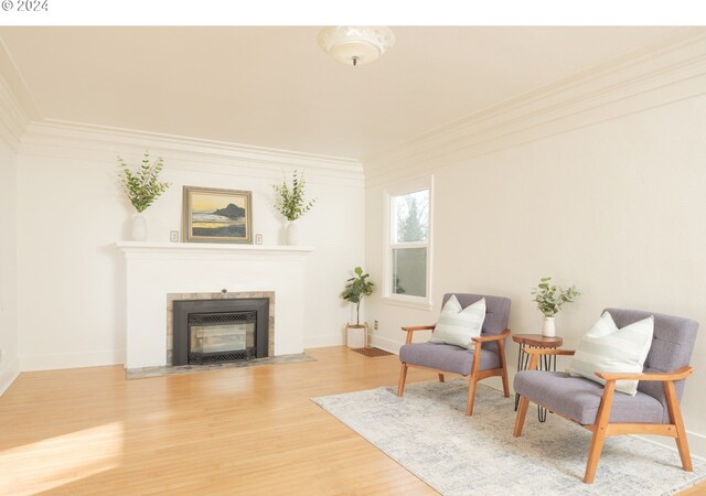 sitting room featuring wood-type flooring, crown molding, and a tiled fireplace