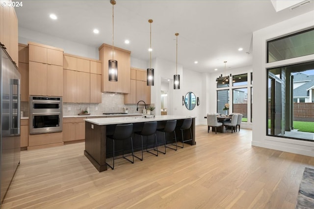 kitchen with appliances with stainless steel finishes, light hardwood / wood-style floors, a kitchen island with sink, and light brown cabinets