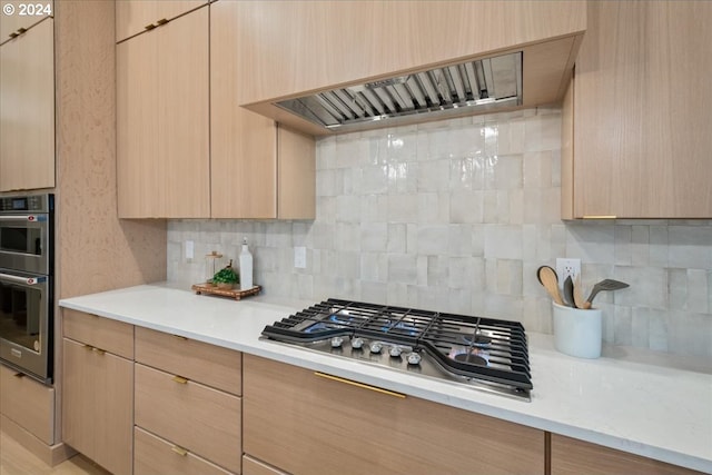 kitchen featuring stainless steel appliances, range hood, light brown cabinetry, and tasteful backsplash