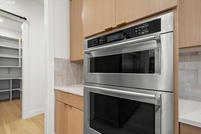 kitchen featuring light brown cabinets, double oven, decorative backsplash, and light hardwood / wood-style floors