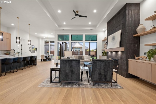 dining room featuring a fireplace, a raised ceiling, ceiling fan, and light hardwood / wood-style flooring