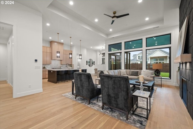 living room featuring ceiling fan, light wood-type flooring, sink, and a tray ceiling