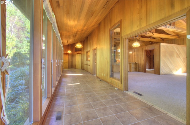 hall featuring wooden walls, light colored carpet, and lofted ceiling