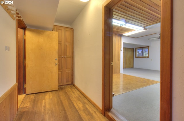 corridor with light wood-type flooring and wooden walls