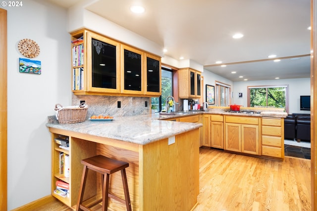 kitchen with light stone countertops, backsplash, kitchen peninsula, sink, and light wood-type flooring