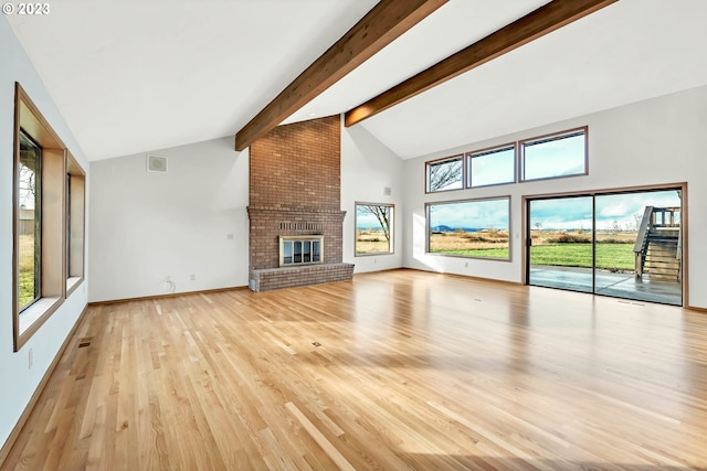 unfurnished living room featuring beamed ceiling, a wealth of natural light, light wood-type flooring, and a brick fireplace