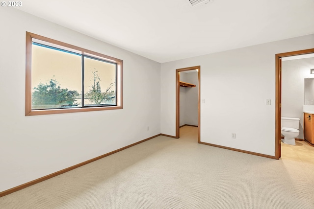 unfurnished bedroom featuring a spacious closet, ensuite bath, light carpet, and a closet