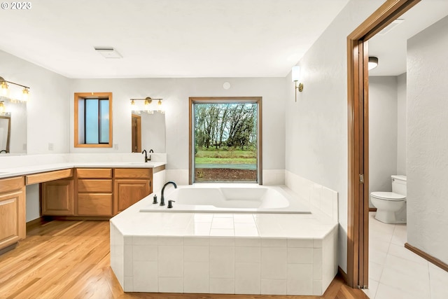 bathroom with vanity, toilet, wood-type flooring, and tiled tub