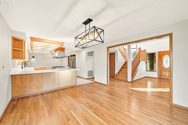 kitchen with sink, kitchen peninsula, hanging light fixtures, light hardwood / wood-style floors, and an inviting chandelier