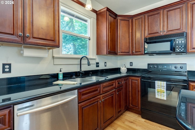 kitchen with black appliances, dark stone countertops, sink, and light hardwood / wood-style flooring