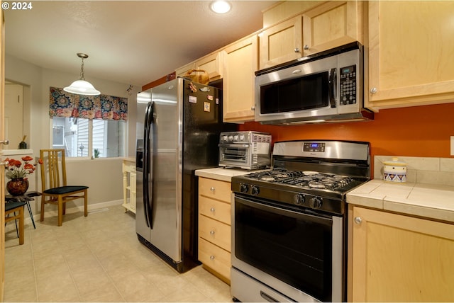 kitchen featuring tile countertops, light brown cabinets, stainless steel appliances, and hanging light fixtures