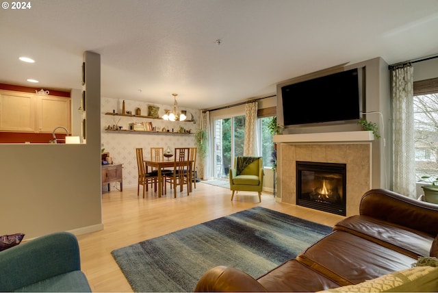 living room featuring a tile fireplace, light wood-type flooring, a chandelier, and sink