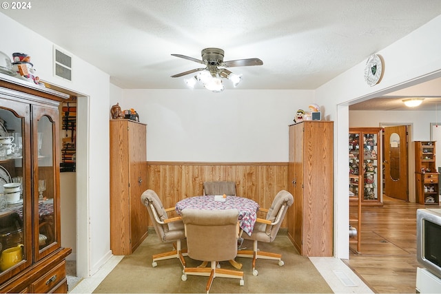 dining room featuring wood walls, ceiling fan, light hardwood / wood-style floors, and a textured ceiling