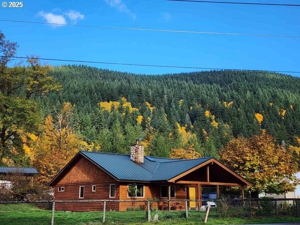 exterior space with metal roof, a fenced front yard, a front lawn, a chimney, and a wooded view