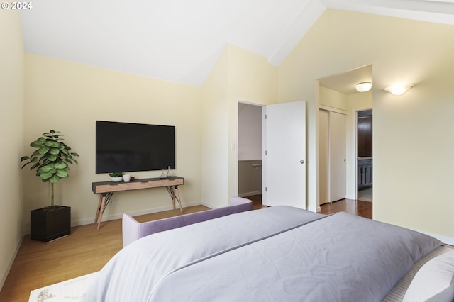 bedroom featuring vaulted ceiling, hardwood / wood-style floors, ensuite bath, and a closet