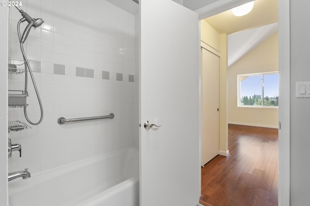 bathroom with wood-type flooring, tiled shower / bath combo, and vaulted ceiling