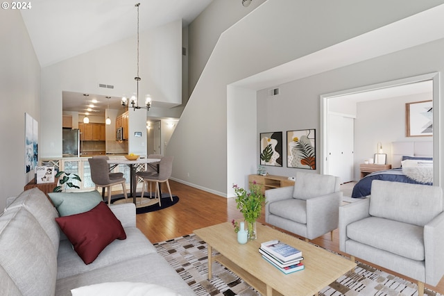 living room featuring high vaulted ceiling, light hardwood / wood-style flooring, and an inviting chandelier