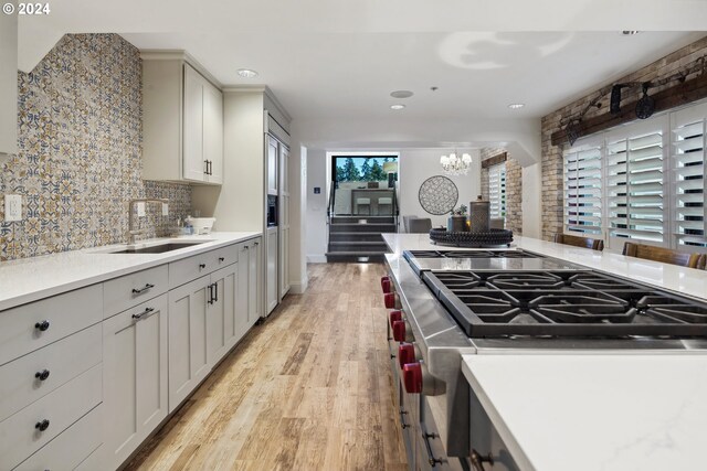 kitchen featuring high end stove, light hardwood / wood-style floors, tasteful backsplash, sink, and an inviting chandelier