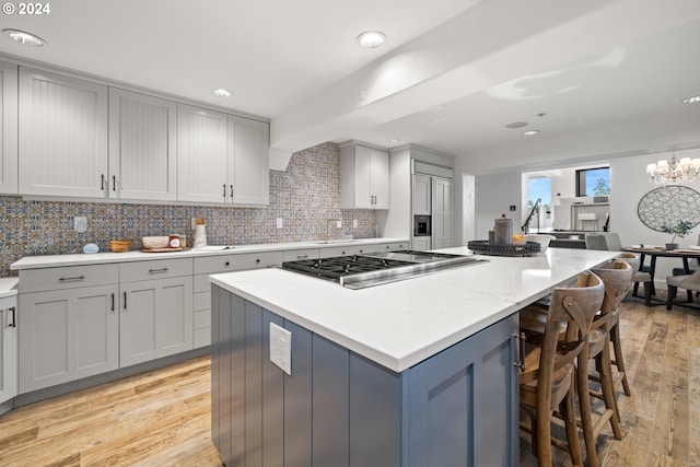 kitchen with light wood finished floors, tasteful backsplash, a breakfast bar area, a center island, and stainless steel gas cooktop