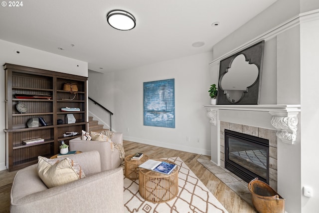 living area featuring baseboards, stairway, a tile fireplace, and light wood-style floors